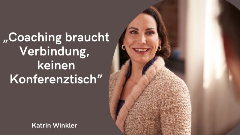 Auf dem Bild ist eine lächelnde Frau mit schulterlangen dunklen Haaren zu sehen, die seitlich nach rechts blickt. Sie trägt eine helle, elegante Jacke mit strukturiertem Stoff und ein dunkles Oberteil darunter. Die Frau wirkt als wäre sie im Gespräch mit einer anderen Person, die im Vordergrund nur unscharf von hinten zu sehen ist. Links im Bild steht auf einem braunen Hintergrund in großer weißer Schrift das Zitat: „Coaching braucht Verbindung, keinen Konferenztisch“ Darunter steht der Name: Katrin Winkler