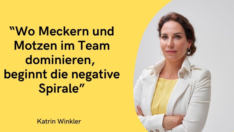 Die linke, größere Hälfte des Bildes hat einen kräftigen, einfarbigen gelben Hintergrund. Darauf ist in großen, schwarzen Druckbuchstaben ein prägnantes Zitat zu lesen: „Wo Meckern und Motzen im Team dominieren, beginnt die negative Spirale“ Ganz unten links auf der gelben Fläche steht in kleinerer, schwarzer Schrift der Name der Urheberin: Katrin Winkler. Auf der rechten Seite geht die gelbe Fläche in einer Kurve in das Porträtfoto über. Das Foto zeigt Katrin Winkler vor einem schlichten, hellgrauen Hintergrund. Sie schaut mit einem ernsten, aber bestimmten und professionellen Gesichtsausdruck direkt in die Kamera. Ihre braunen Haare sind nach hinten gesteckt, und sie trägt Ohrringe. Bekleidet ist sie mit einem gelben Oberteil, das farblich exakt auf den linken Hintergrund abgestimmt ist, und einem eleganten, weißen Blazer mit Kragen. Ihre Arme hat sie verschränkt, was der Aufnahme eine selbstbewusste und fokussierte Wirkung verleiht.